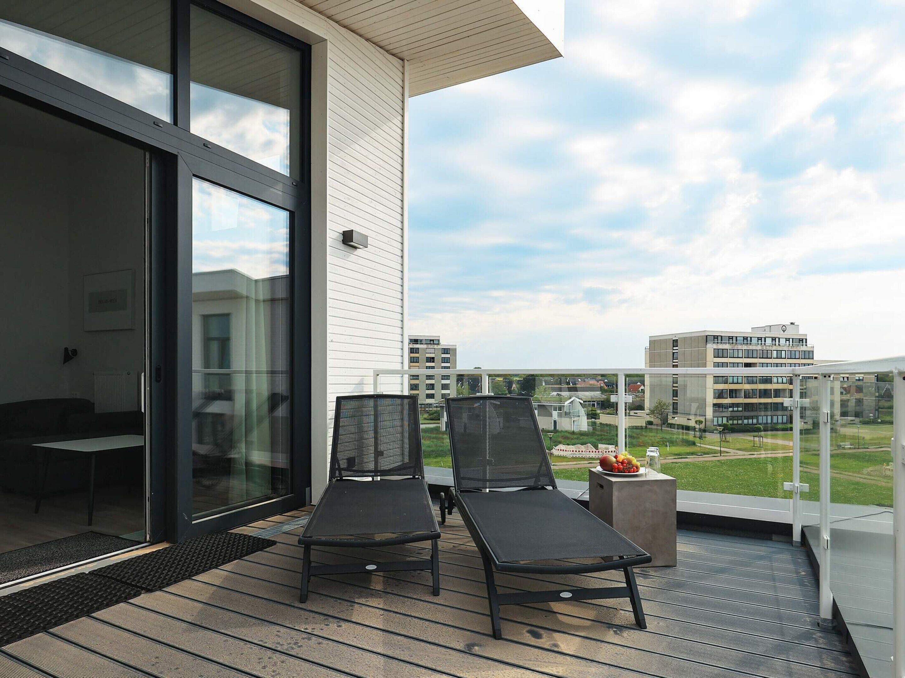 A balcony with two lounge chairs, a small table with fruit, and a view of surrounding buildings.
