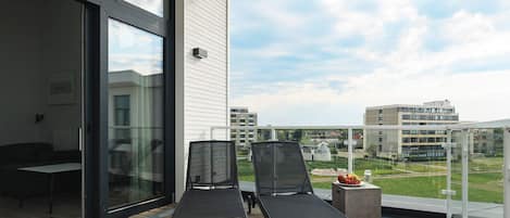 A balcony with two lounge chairs, a small table with fruit, and a view of surrounding buildings.