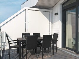 Una terraza con mesa y sillas, una puerta corredera de vidrio y una pared exterior blanca.