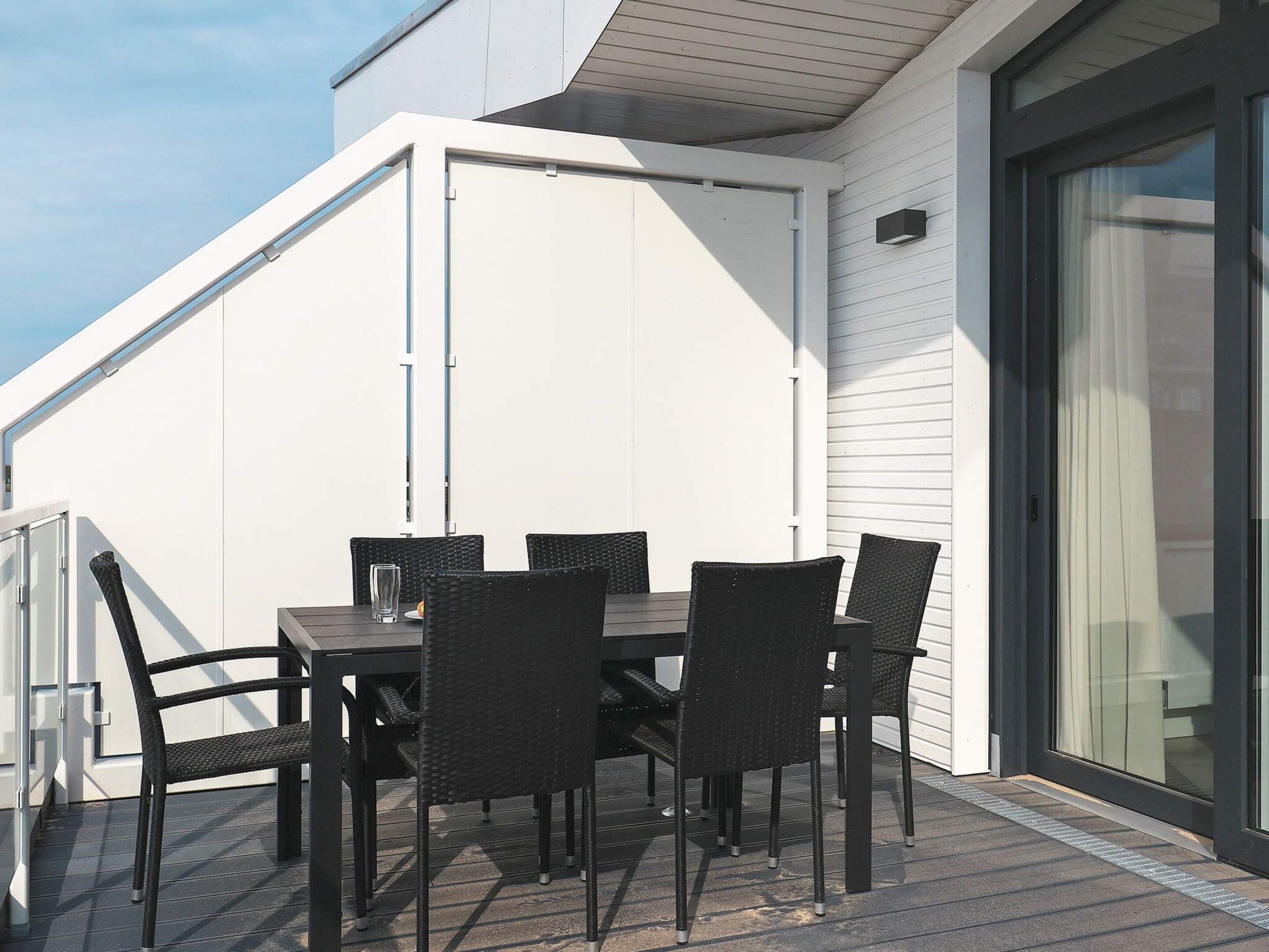 A terrace with a table and chairs, a sliding glass door, and a white exterior wall.