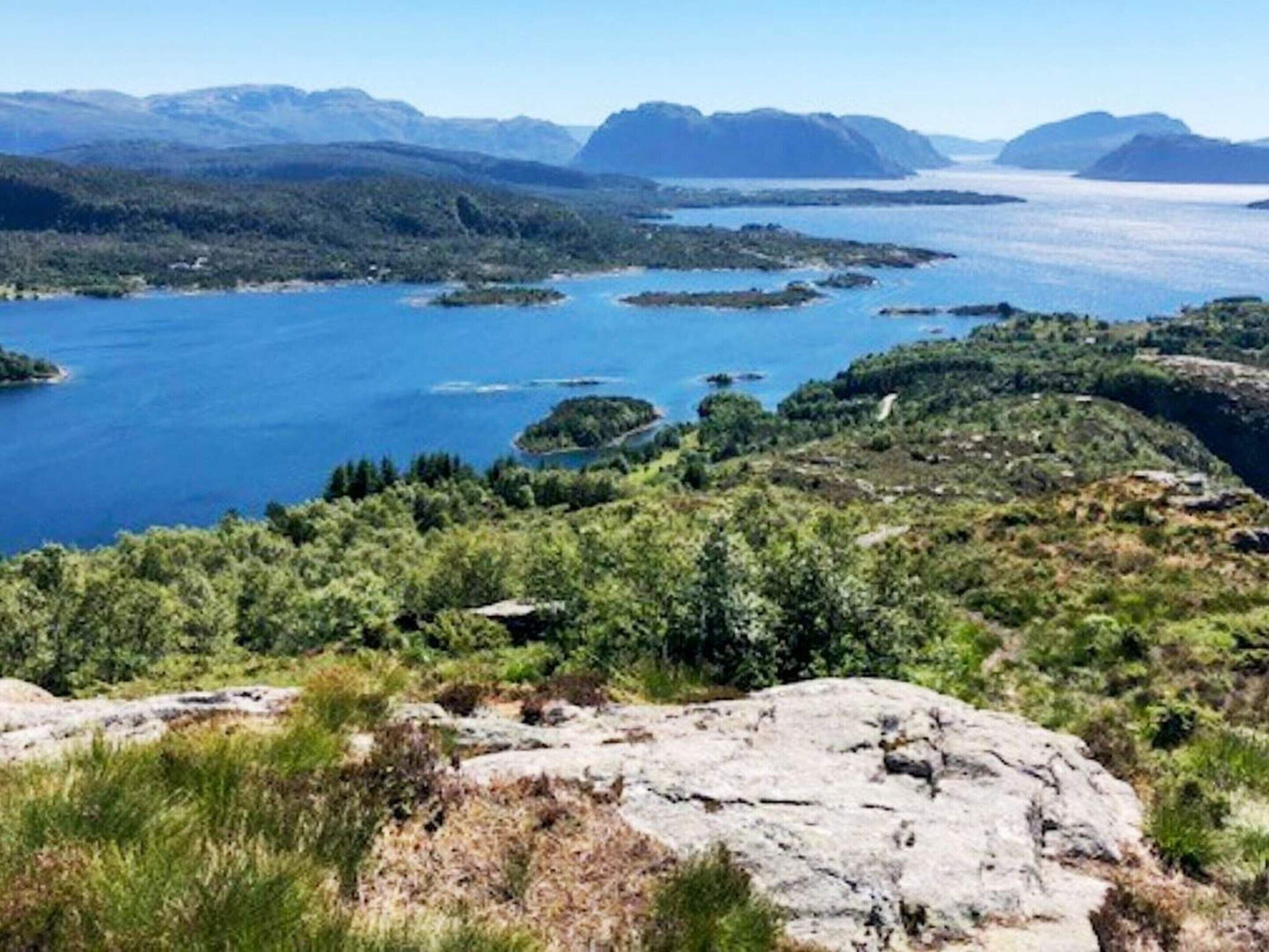 Un paisaje costero con una extensa masa de agua, terreno rocoso y montañas al fondo.