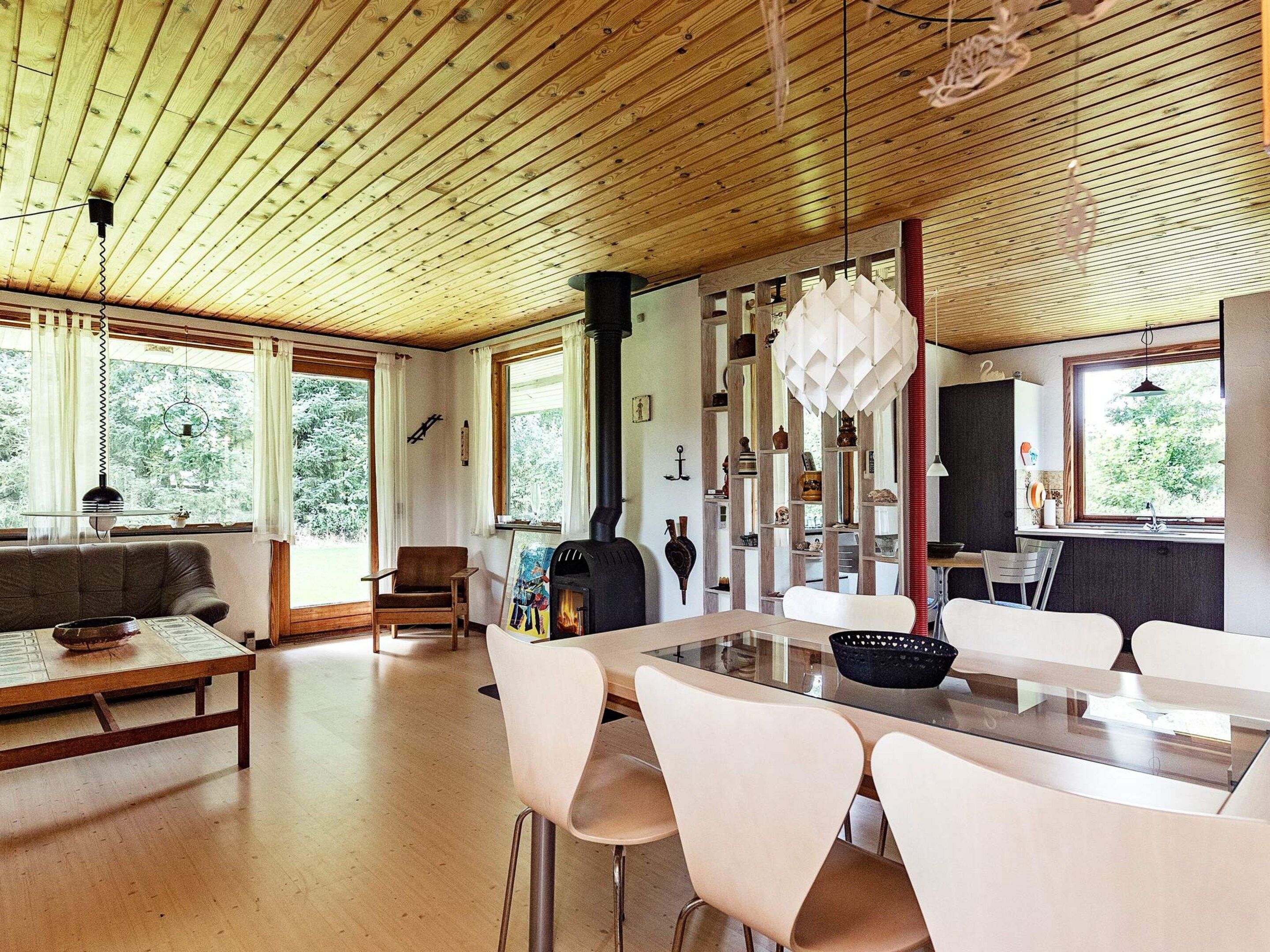 Un interior moderno con techo de madera, una zona de comedor con mesa de cristal y una chimenea.