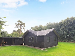 A small, dark-colored wooden building with a sloped roof, a door, and windows, situated on a grassy area with trees in the background. - 6 Person Holiday Home in Oster Assels (Øster Assels)