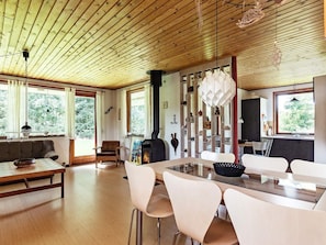 En modern inredning med ett träpanelat tak, en matplats med ett glasbord och ett kök med en inbyggd spis.
