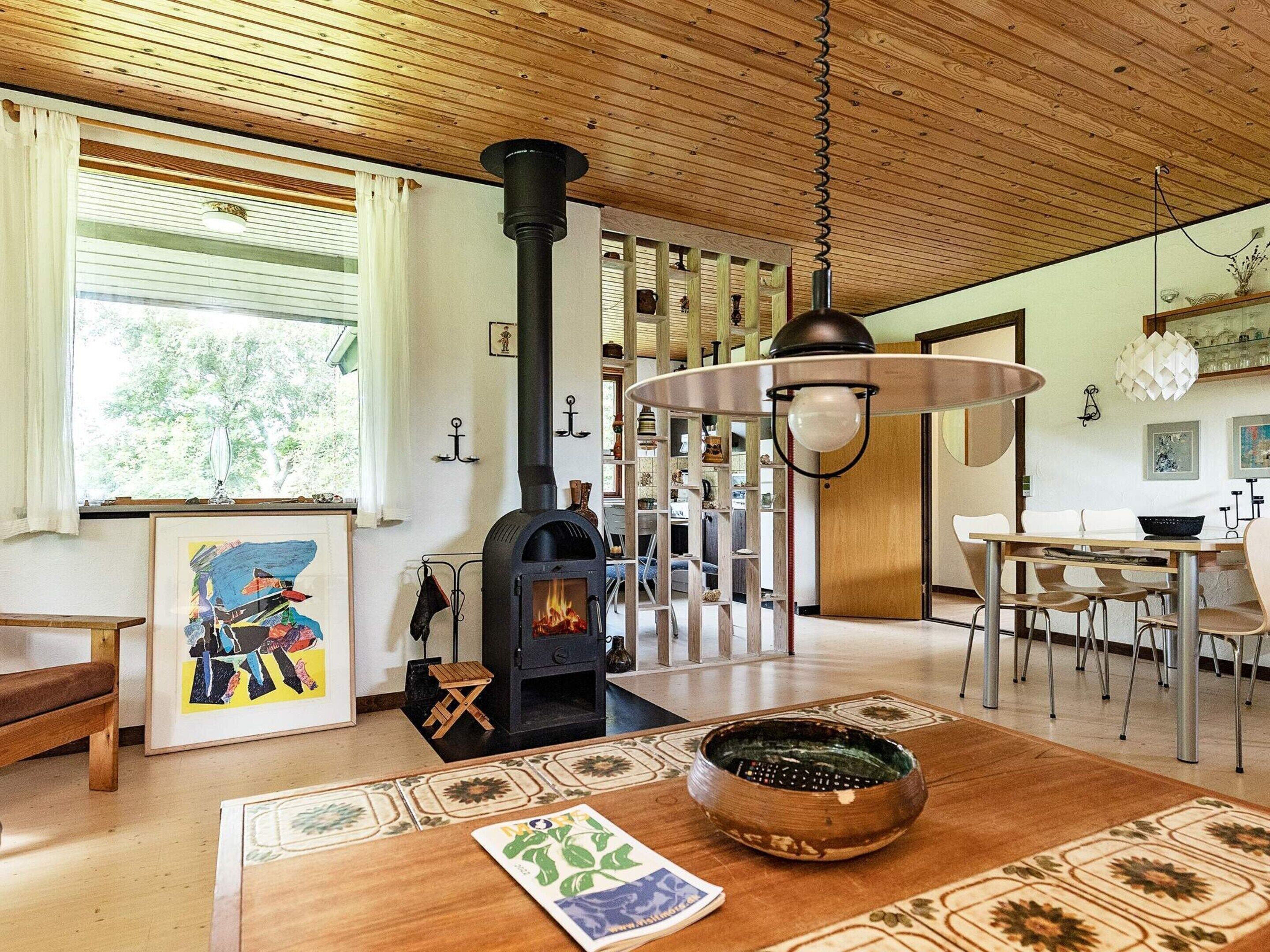 A cozy living room with a fireplace, wooden ceiling, and a dining area with a table and chairs.