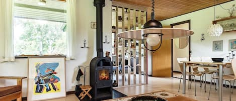 A cozy living room with a fireplace, wooden ceiling, and a dining area with a table and chairs.
