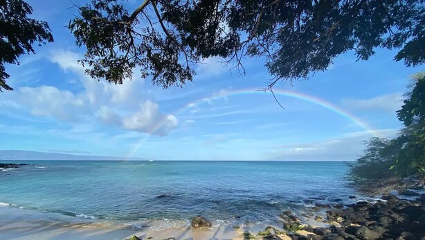 Ein Strand mit Regenbogen, felsigem Ufer und ruhiger See.