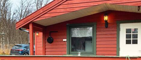 A red wooden house with a porch, a garage door, and a car parked outside.