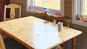Een houten eettafel met stoelen, een raam met uitzicht op de omgeving, en een fles handdesinfectiemiddel op de tafel.