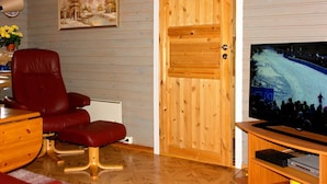 Een woonkamer met een rode leren bank, houten vloeren, een televisie en een houten deur.