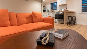 Ein modernes Wohnzimmer mit einem orangefarbenen Sofa, einem Couchtisch aus Holz mit einer Fernbedienung, einem Buch und einer Perlenkette.