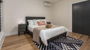Ein Schlafzimmer mit Bett, Nachttischen, Deckenventilator, Klimaanlage, dunklem Wandschrank und einem gemusterten Teppich.