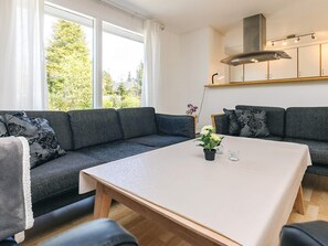 A modern living room with a grey sofa set, a white coffee table, and a large window with a view of greenery.