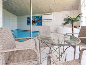 A pool area with wicker chairs and a glass table, a painting on the wall, and a potted plant. - 14 Person Holiday Home in Vaeggerlose (Vaeggerlose)