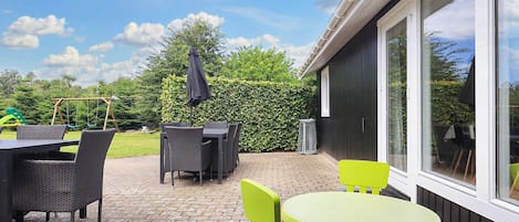 Un patio exterior con una mesa, sillas, un columpio y un seto.