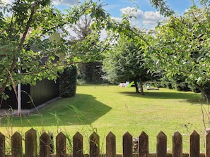 A well-maintained grassy area with a wooden fence, trees, and a playground in the background.