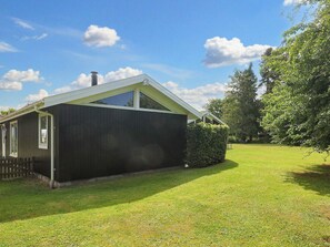 A single-story building with a dark exterior, a sloped roof, and a small front yard with a hedge.