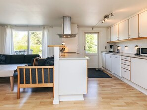 A compact kitchen with a central island, a dining area with a sofa, and a view of greenery outside.