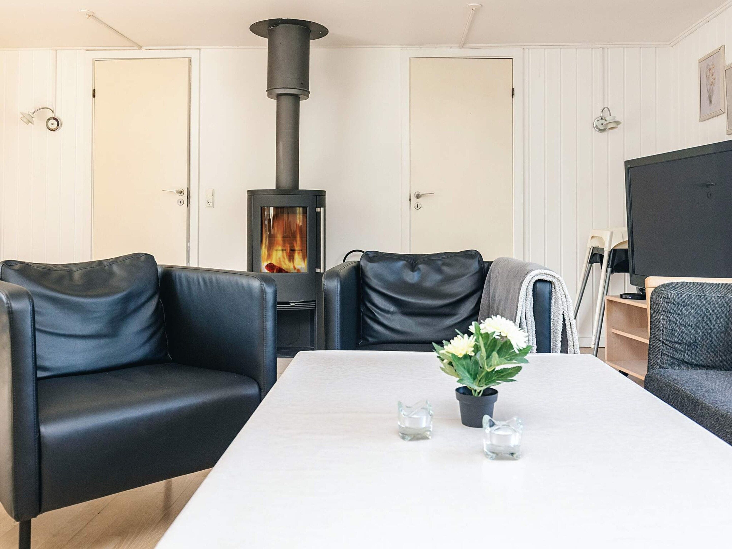 A living room with a black wood-burning stove, leather sofas, a white table, and a potted plant.