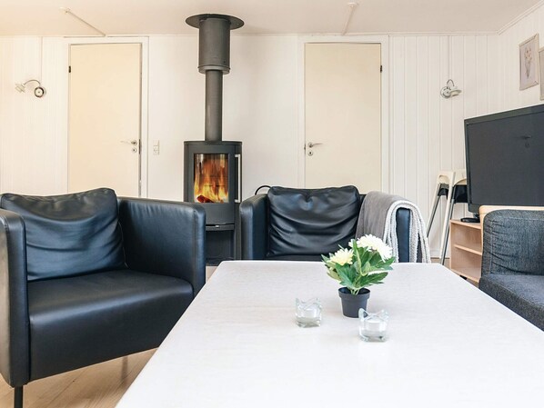 A living room with a black wood-burning stove, leather sofas, a white table, and a potted plant.