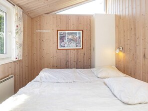 A room with wooden panel walls, a bed with white bedding, a framed picture on the wall, and a window with floral curtains. - 14 Person Holiday Home in Vaeggerlose (Vaeggerlose)