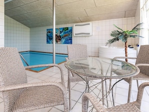 A pool area with wicker chairs and a glass table, a painting on the wall, and a potted plant.