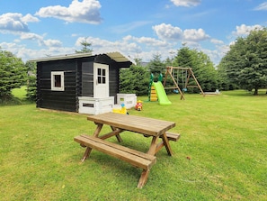 A wooden picnic table in a grassy yard with a play area including a slide and swings in the background.