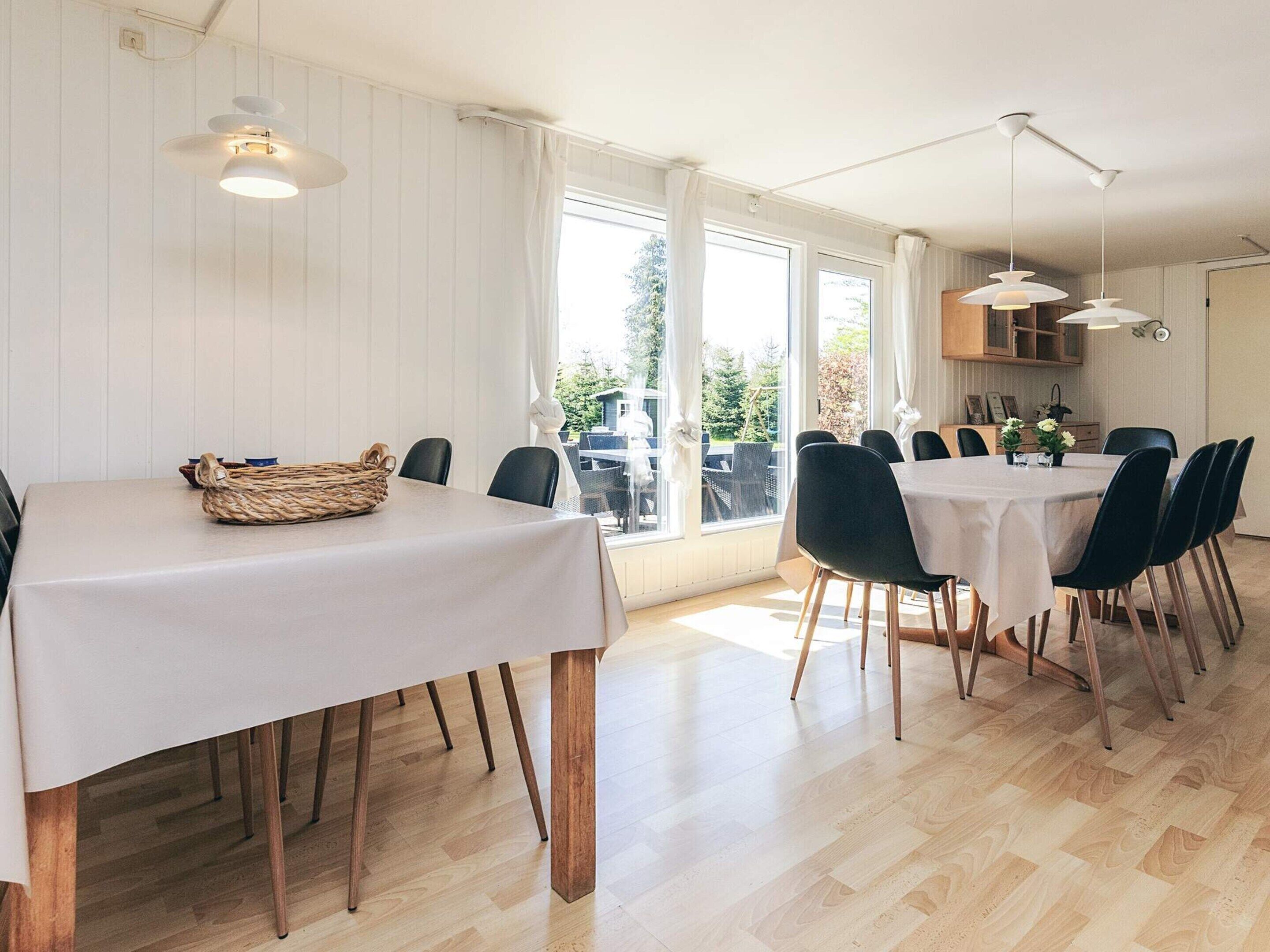 Ein Essbereich mit einem Tisch für sechs Personen, Holzboden und großen Fenstern mit Blick ins Freie.