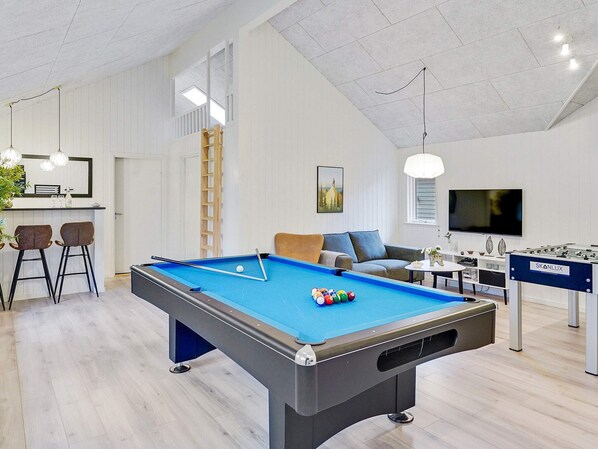 A modern indoor recreational area with a pool table, a foosball table, and a bar area with stools.
