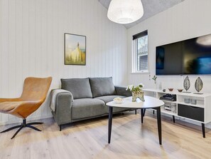 A modern living room with a grey sofa, a brown leather chair, a white coffee table, and a flat-screen TV on a white stand. - 5 Star Holiday Home in Vaeggerlose (Vaeggerlose)