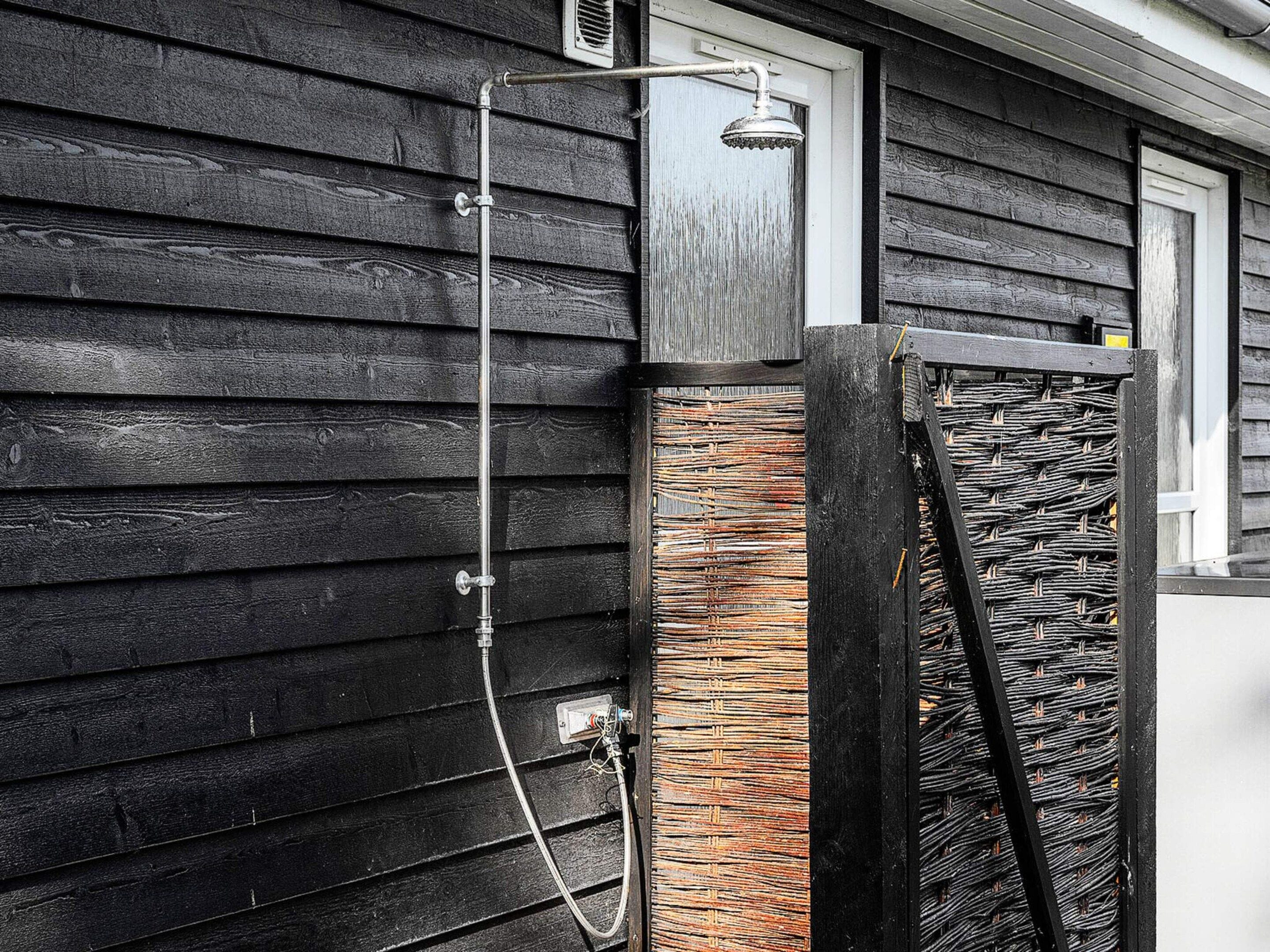 Pared exterior de madera con un tubo de metal y un cabezal de ducha.