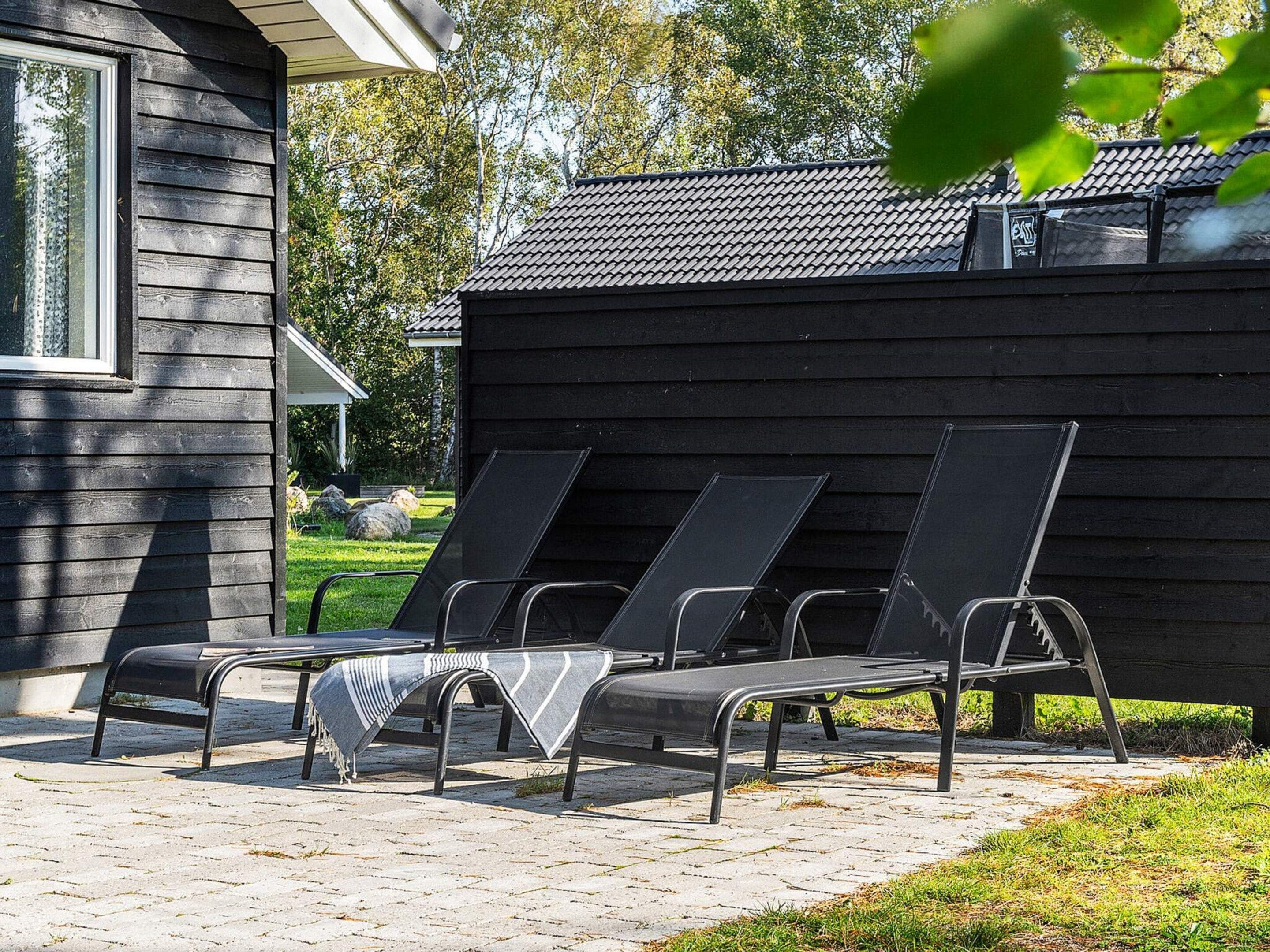 A row of black lounge chairs with metal frames and a blanket on one.