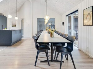 A modern dining area with a long table, black chairs, and pendant lighting.