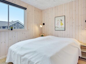 A bedroom with a large bed, wooden panel walls, a window with a view of houses, and a framed picture on the wall. - 5 Star Holiday Home in Vaeggerlose (Vaeggerlose)