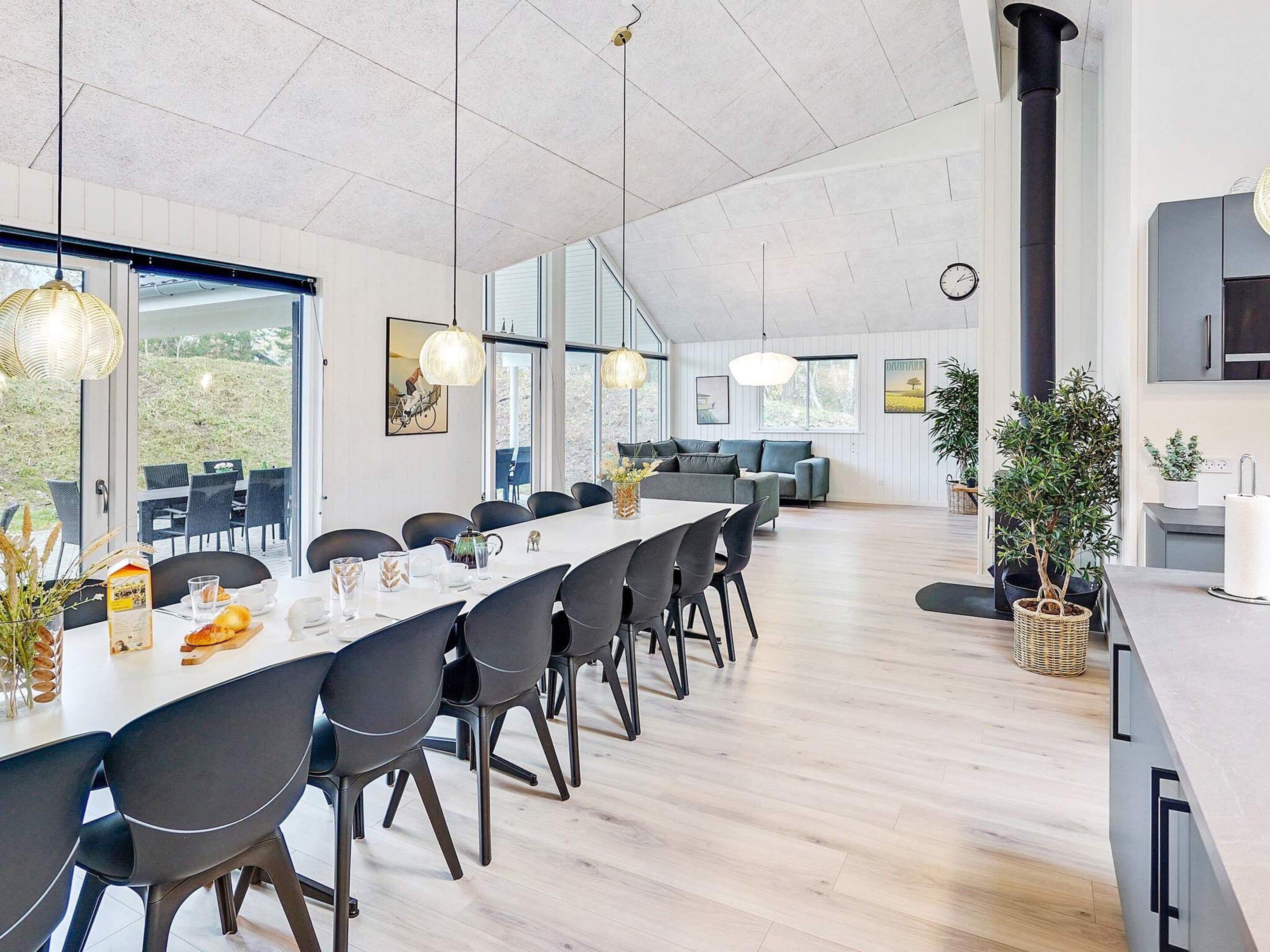 Uma área de jantar moderna com uma mesa comprida, cadeiras e luminárias pendentes.