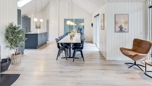 A modern dining area with a long table, chairs, pendant lights, and a view of the kitchen. - 5 Star Holiday Home in Vaeggerlose (Vaeggerlose)