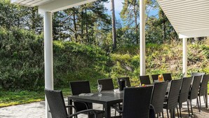 An outdoor patio with a table and chairs, surrounded by greenery and trees. - 5 Star Holiday Home in Vaeggerlose (Vaeggerlose)