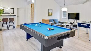 Un área recreativa moderna en interiores con mesa de billar, mesa de futbolín y zona de bar con taburetes.