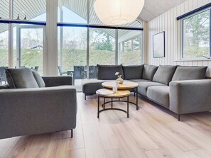 Un salon moderne avec un canapé d’angle, une table basse ronde et une vue sur l’extérieur grâce à de grandes fenêtres.