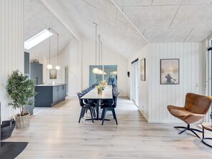 Un espace de salle à manger moderne, avec une longue table, des chaises, des luminaires suspendus et une vue à travers une porte vitrée.