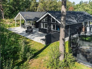 Une maison moderne dotée d’un patio couvert, d’une cour clôturée et d’une grande fenêtre.