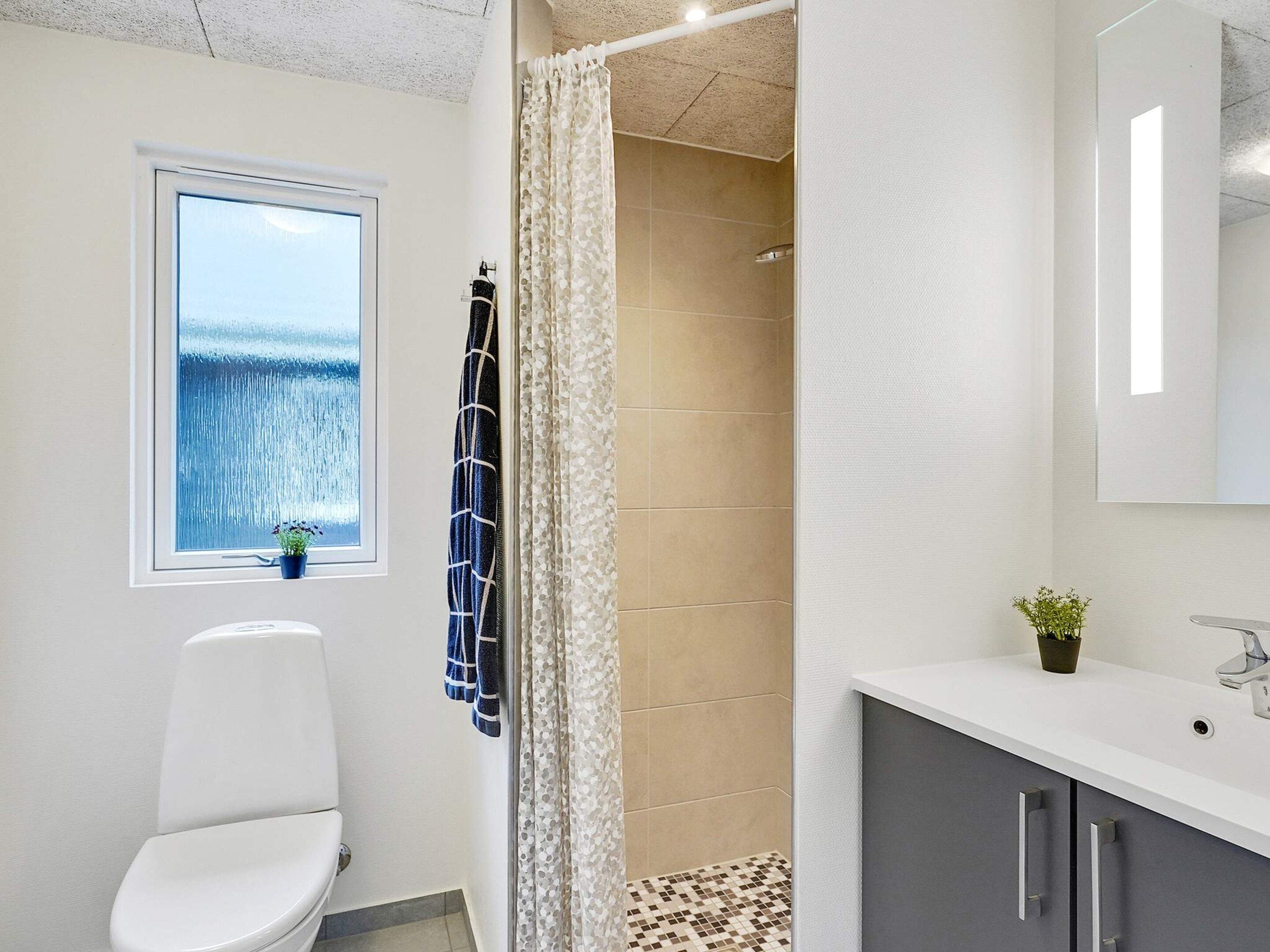 Une salle de bain comprenant des toilettes, une douche avec un rideau, un lavabo avec un miroir et une fenêtre donnant sur la mer.