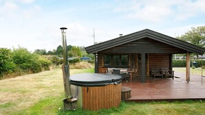 A wooden cabin with a deck, a hot tub, and a grill.
