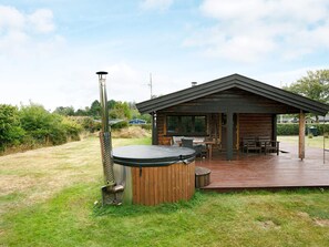 A wooden cabin with a deck, a hot tub, and a grill.