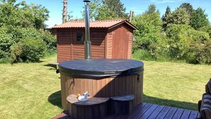 A hot tub on a wooden deck with a small wooden cabin in the background.