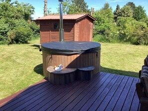 A hot tub on a wooden deck with a small wooden cabin in the background.