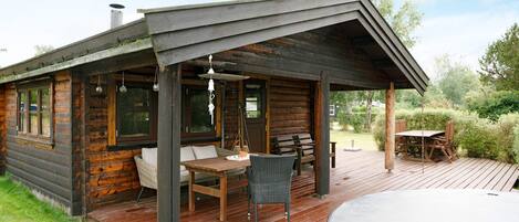 A log cabin with a deck, outdoor seating, and a hot tub.