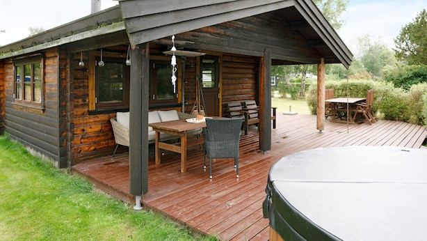 A wooden cabin with a deck, a hot tub, and outdoor seating.