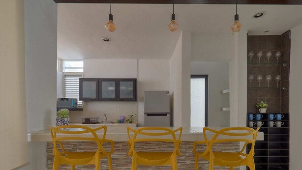 A modern kitchen with a central island, three yellow chairs, and hanging pendant lights. - Casita el Pinar - Yucatan Home Rentals (Mérida)