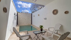 A small outdoor patio with a pool, two white plastic chairs, a glass table, and a ceiling fan. - Casita el Pinar - Yucatan Home Rentals (Mérida)